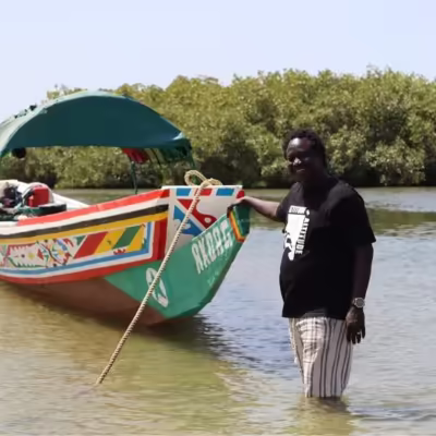 Diambar, guide indépendant, aux côtés d'une pirogue traditionnelle dans les mangroves du Sine Saloum