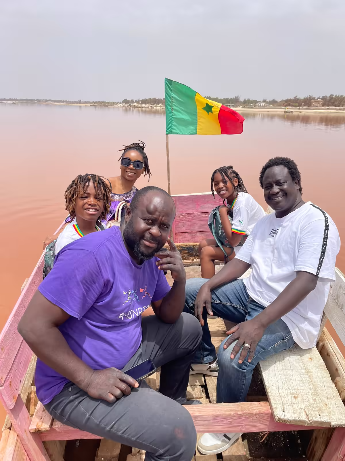 Groupe de voyageurs en pirogue sous le drapeau sénégalais sur les eaux roses du Lac Retba