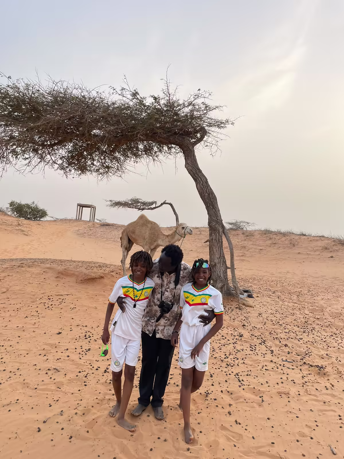Jeunes voyageurs en maillot du Sénégal posant près d'un dromadaire dans le désert de Lompoul